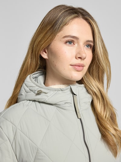 Frauenmodel trägt Steppjacke mit Zweiwege-Reißverschluss von camel active, helle Farbe, sichtbare Steppstruktur, Nahaufnahme Oberkörper. Gerade Passform, Kapuze mit Tunnelzug, Kinnschutz, Eingrifftaschen, elastische Ärmelabschlüsse, Rückenlänge 71 cm, Schulterbreite 48 cm, Brustweite 56 cm, Ärmellänge 58 cm.