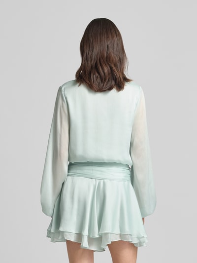 Frauenmodel trägt Minikleid mit kurzer Knopfleiste Modell 'MAGALI' von Guess in hellblau mit Volantsaum, Taillierter Schnitt, Rückenansicht.