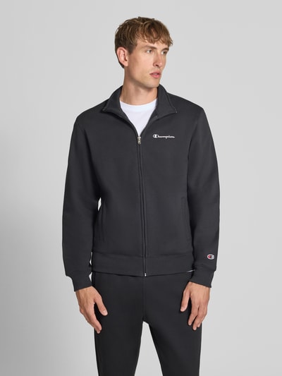 Męski model nosi Sweatanzug mit Label-Details od Champion, czarny, mieszanka bawełny, prosty krój, stójka, zamek błyskawiczny, detale z logo, wpuszczane kieszenie boczne, elastyczny pas, Szerokość w rozmiarze M: 76,42 cm, Długość tyłu w rozmiarze M: 70 cm, Szerokość ramion w rozmiarze M: 51 cm, Długość rękawów w rozmiarze M: 69 cm, Długość wewnętrzna nogawki w rozmiarze M: 76 cm, widok całej sylwetki od przodu