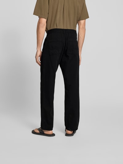 Männermodel trägt schwarze Straight Fit Jeans mit elastischem Bund von Forét aus reiner Baumwolle, Gesäßtaschen, Ganzkörperansicht Rückansicht.