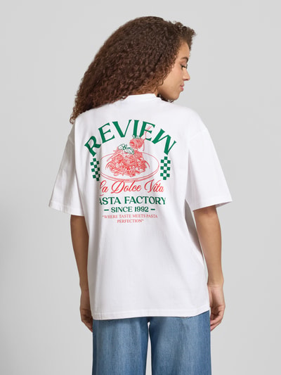 Frauenmodel trägt Damen T-Shirt mit rückseitigem Motiv-Print von REVIEW, weiße reine Baumwolle, Oversized, Rundhalsausschnitt, Rückenlänge 68 cm, Ganzkörperansicht Rückansicht.