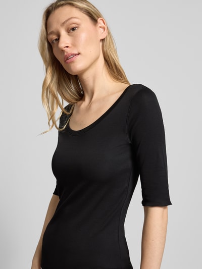 Kobiece model prezentuje T-Shirt mit Ärmelaufschlag und Rundhalsausschnitt von Marc Cain, mieszanka bawełny, z dodatkiem streczu, dopasowany krój, okrągły dekolt, rękawy z zakładką, detal z logo, długość tyłu w rozmiarze 36: 60 cm, kolor czarny, gładka tekstura, prosty fason, z przodu, zbliżenie na górną część ciała.