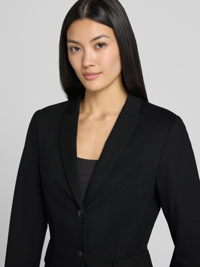Vrouwenmodel draagt Slim Fit Blazer aus Viskose-Mix van Marc Cain in zwart, mix van viscose en elastaan, reverskraag, 2-knoopsluiting, klepzak, borstwijdte maat 36: 23 cm, mouwlengte maat 36: 63 cm, ruglengte maat 36: 56 cm, nahaufnahme bovenlichaam.