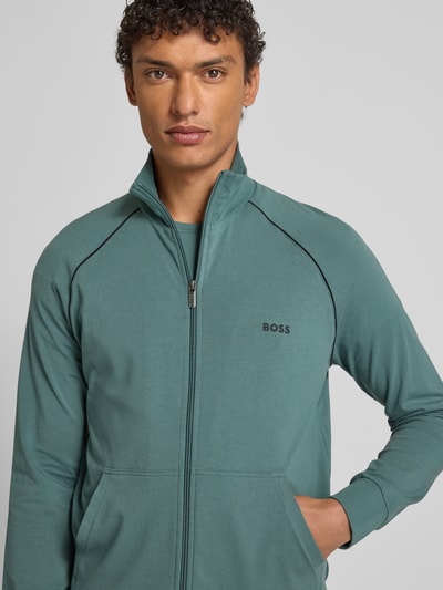 Męski model nosi Regular Fit bluzę rozpinaną z mieszanki bawełny Model 'MIX&MATCH JACKET Z' od BOSS, jednokolorowa, zamek błyskawiczny, wyhaftowane logo, paski w kontrastowym kolorze, stójka, długi rękaw, kieszeń kangurka, materiał: mieszanka bawełny, kolor zielony, z przodu, zbliżenie na górną część ciała.