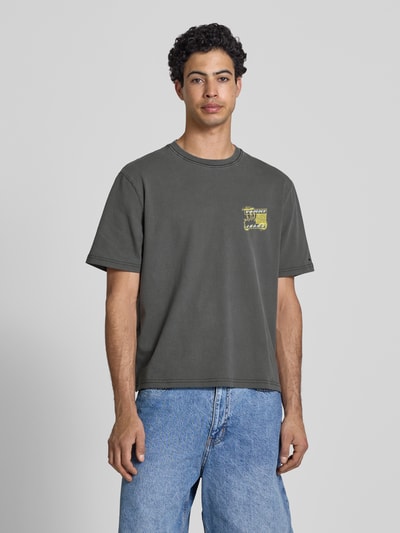 Männermodel trägt Regular Fit T-Shirt aus reiner Baumwolle Modell '90s' von Tommy Jeans in Unifarben mit Label Print, Ganzkörperansicht von vorne.