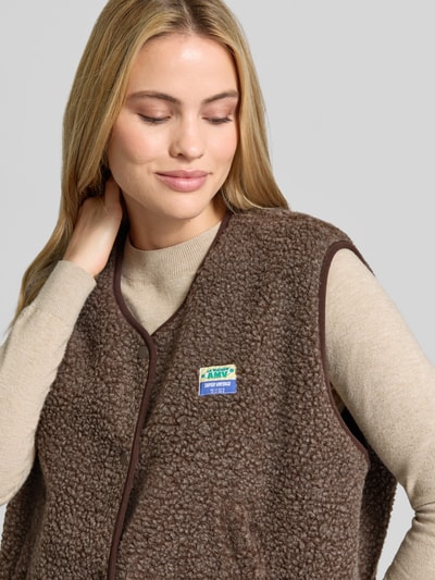 Frauenmodel trägt Relaxed Fit Weste aus Teddyfell Modell 'Hoktown' von American Vintage, braun mit Logo-Patch, Nahaufnahme Oberkörper. Damen Weste, Teddyfell, Relaxed Fit, Knopfleiste, Rückenlänge 56 cm, Schulterbreite 43 cm, Brustweite 63 cm.