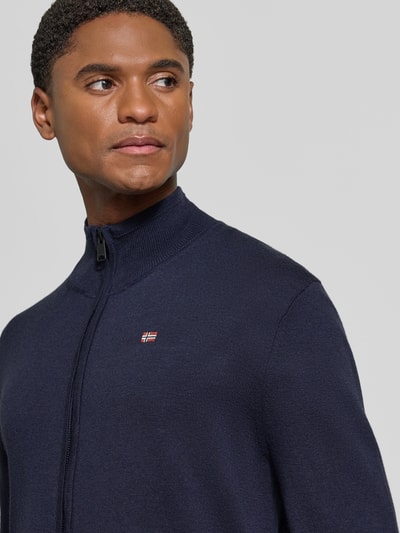 Männermodel trägt Strickjacke mit Logo-Stitching Modell 'DAMAVAND' von Napapijri in Dunkelblau, Reißverschluss, Nahaufnahme Oberkörper. Reine Wolle, Regular Fit, gerippter Stehkragen.