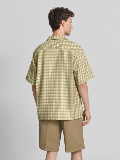 Männermodel trägt Regular Fit Freizeithemd aus reiner Baumwolle von Carhartt Work In Progress mit Strukturmuster, kariert, Halbarm, Ganzkörperansicht Rückansicht. Rückenlänge bei Größe M: 74 cm, Schulterbreite bei Größe M: 49 cm, Ärmellänge bei Größe M: 29 cm, durchgehende Knopfleiste, Brand-Stitching.