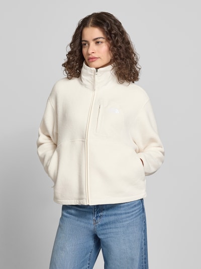 Frauenmodel trägt Fleecejacke mit Stehkragen und Label-Stitching von The North Face in Creme mit Reißverschluss, Brusttasche, Regular-Fit, Ganzkörperansicht von vorne. Rückenlänge bei Größe S: 57 cm, Schulterbreite: 50 cm, Brustweite: 56 cm, Ärmellänge: 56 cm.