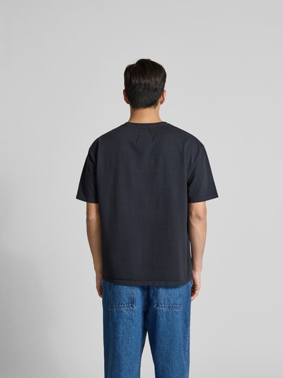 Männermodel trägt Regular Fit T-Shirt aus reiner Baumwolle von RHUDE in Dunkelgrau mit Label-Print, Rückenlänge 70 cm, Ganzkörperansicht Rückansicht.