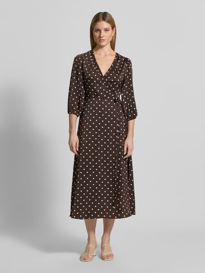 Frauenmodel trägt Regular Fit Maxikleid mit V-Ausschnitt von Neo Noir aus braunem Satin mit weißen Punkten, Wickel-Optik, 3/4-Arm, elastische Ärmelabschlüsse und Raffungen, Ganzkörperansicht von vorne.