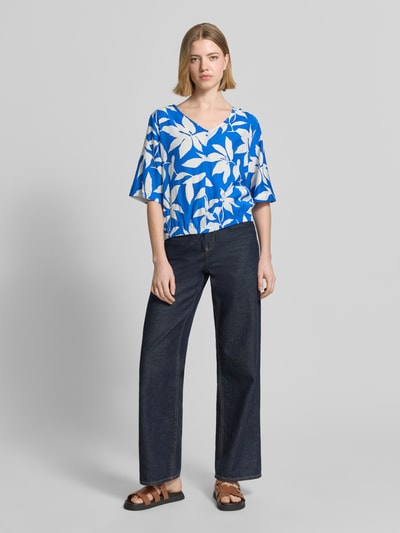 Frauenmodel trägt Relaxed Fit Blusentop aus Viskose-Mix von s.Oliver RED LABEL mit floralem Allover-Muster in Blau und Weiß, Satinoptik, Ganzkörperansicht von vorne.