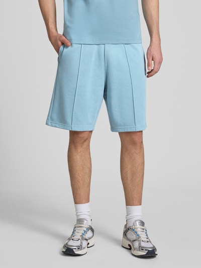 Mężczyzna nosi Bermudas mit elastischem Bund und Label-Stitching von CHAMPION z mieszanki bawełny, krój regular fit, jasnoniebieski, długość nogawki 24 cm, szerokość w rozmiarze M 42 cm, z wyhaftowanym logo, widok od przodu, ujęcie całej sylwetki.