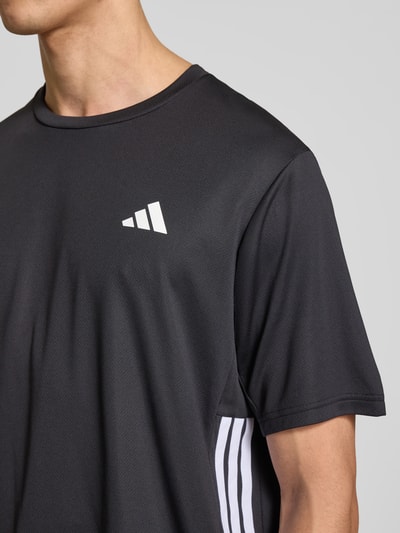 Männermodel trägt Regular Fit T-Shirt mit Logo-Print von adidas Training in Optik: Unifarben mit Kontraststreifen, Rundhals, Nahaufnahme Oberkörper.