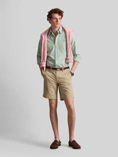 Męski model nosi Straight Fit Chinoshorts aus Baumwoll-Mix von Polo Ralph Lauren, efekt: jednolity kolor, krój straight fit, detal z logo, szlufki na pasek, zapięcie na guzik i ukryty zamek błyskawiczny, tylne kieszenie, wpuszczane kieszenie, mieszanka bawełny, całkowity widok z przodu.