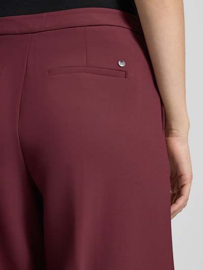 Frauenmodel trägt Wide Fit Hose mit Bügelfalten Modell 'Leya' von MOS MOSH in Bordeaux, glatte Textur, Detailaufnahme, Bundweite 62 cm, Innenbeinlänge 80 cm.