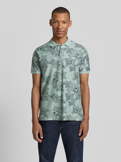 Männermodel trägt Slim Fit Poloshirt mit floralem Allover-Print von Lerros aus Reine Baumwolle, mintgrün mit schwarzen Blütenmotiven, Polokragen, kurzärmelig, Rückenlänge bei Größe M 72 cm, Ganzkörperansicht von vorne.