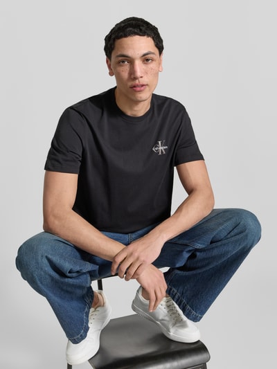 Männermodel trägt T-Shirt mit Rundhalsausschnitt und Logo von Calvin Klein Jeans in Schwarz, reine Baumwolle, Regular Fit, Nahaufnahme Oberkörper.