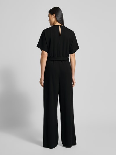 Frauenmodel trägt schwarzen Jumpsuit mit Bindegürtel Modell 'Renata' von GUIDO MARIA KRETSCHMER WOMAN, weiter Schnitt, Ganzkörperansicht Rückansicht.