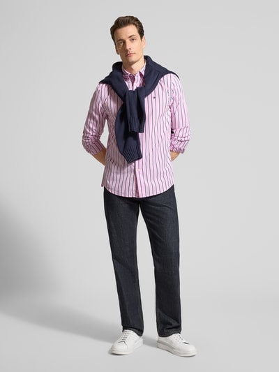 Męski model nosi Regular Fit Freizeithemd aus reiner Baumwolle von Tommy Hilfiger, paski, różowy z granatem, widok całej sylwetki z przodu.