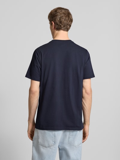 Męski model nosi Regular Fit T-Shirt mit Logo-Patch od Carhartt Work In Progress, granatowa bawełna, widok całej sylwetki z tyłu.
