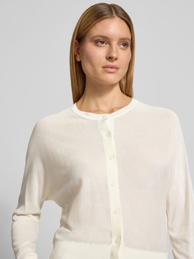 Modelka kobieca nosi kardigan rozpinany z mieszanki wiskozy, krój regular fit, model 'Desela' od OPUS, okrągły dekolt, listwa guzikowa, kremowy kolor, tekstura gładka, damski kardigan, długość tyłu 54 cm, długość rękawów 52 cm, rozmiar 36, zbliżenie na górną część ciała, ujęcie z przodu