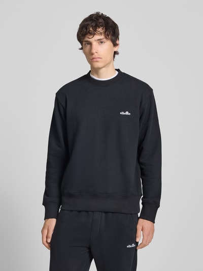 Männermodel trägt Sweatshirt mit Rundhalsausschnitt und Label-Stitching von Ellesse, schwarze Farbe, Regular Fit, Baumwoll-Mix, Ganzkörperansicht von vorne