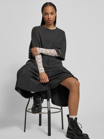 Frauenmodel trägt Oversized T-Shirt mit Label-Stitching von black palms aus reiner Baumwolle im Destroyed-Look, Rundhalsausschnitt, Rückenlänge 77 cm, schwarze Farbe, glatte Struktur, Ganzkörperansicht von vorne.