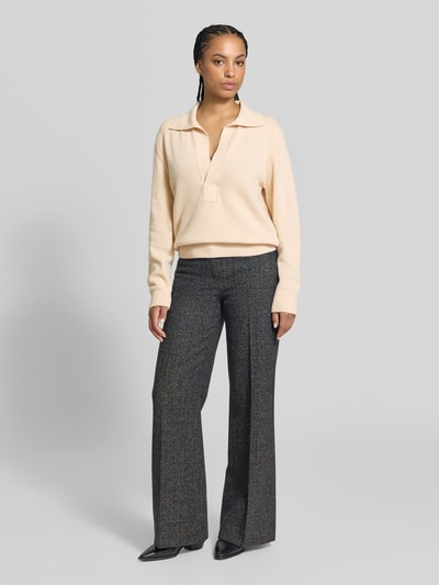Frauenmodel trägt Relaxed Fit Pullover aus Woll-Mix von Victoria Beckham in Creme mit Strick-Optik, Umlegekragen, V-Ausschnitt, Ganzkörperansicht von vorne.