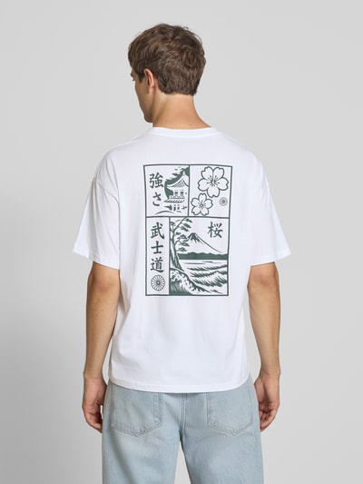 Männermodel trägt Relaxed Fit T-Shirt aus reiner Baumwolle Modell "DYLAN" von JACK & JONES mit Print-Detail auf weiß, Ganzkörperansicht Rückansicht.