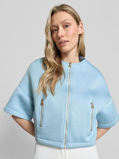 Frauenmodel trägt Jacke mit 1/2-Arm und Reißverschlusstaschen von Rinascimento in Hellblau, glänzende Reißverschlüsse, Struktur glatt, Nahaufnahme Oberkörper.