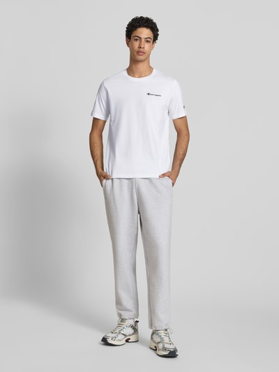 Männermodel trägt T-Shirt mit Label-Stitchings und Rundhalsausschnitt von CHAMPION, Reine Baumwolle, Regular-Fit, Herren T-Shirt, Ganzkörperansicht von vorne. Rückenlänge bei Größe M: 69 cm.