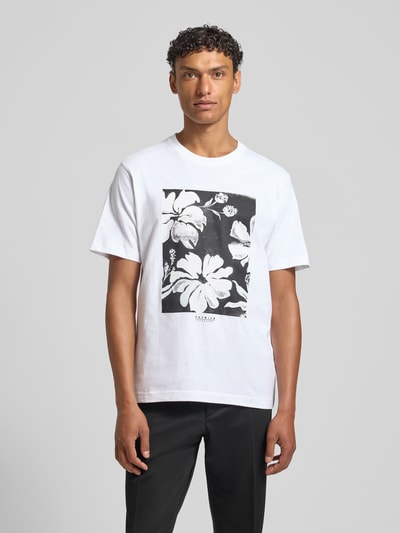 Männermodel trägt Herren T-Shirt mit Motiv-Print Modell 'LUCAS' von Jack & Jones Premium, Reine Baumwolle, Slim-Fit, Rundhalsausschnitt, schwarz-weißes Blumenmotiv, Rückenlänge bei Größe M: 67 cm, Ganzkörperansicht von vorne.