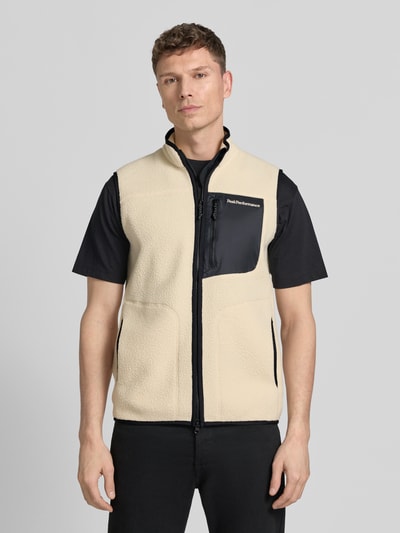 Männermodel trägt Weste mit Brusttasche Modell 'NatureRush' von PEAK PERFORMANCE in Beige mit schwarzer Brusttasche, Stehkragen, Fleece, gerader Schnitt, Logo-Stitching, Zweiwege-Reißverschluss, Ganzkörperansicht von vorne.