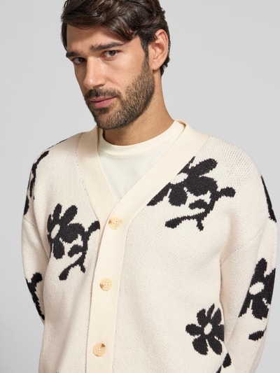Männermodel trägt Strickjacke im Allover-Look Modell 'DIA INTARCIA' von Casual Friday, cremefarben mit schwarzen Blumenmustern, Material-Mix mit Woll-Anteil, Knopfleiste und V-Ausschnitt, Relaxed Fit, Nahaufnahme Oberkörper.