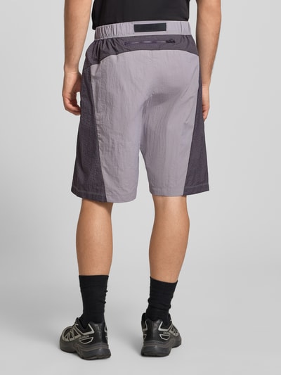 Mężczyznamodel nosi Shorts mit Logo und Gürtel od The North Face, kolor szary, pasek, logo, elastyczny pas, krój regular fit, szerokość w rozmiarze M 42 cm, długość nogawki w rozmiarze M 24 cm, widok całej sylwetki z tyłu.