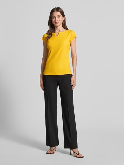 Modelka nosi T-Shirt mit Cut Out od Marc Cain, żółty kolor, prosty krój, okrągły dekolt, cienki prążkowany materiał z domieszką stretchu, widok całej sylwetki z przodu, długość tyłu w rozmiarze 36: 56 cm.