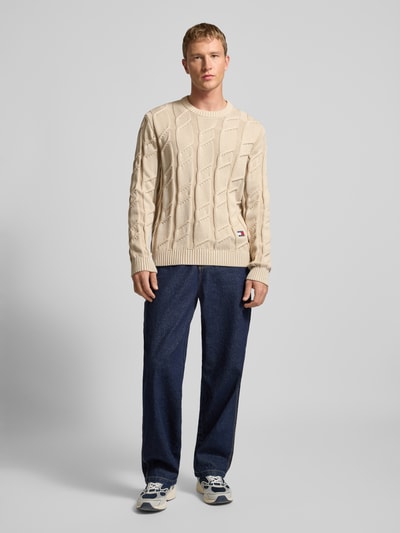 Männermodel trägt Regular Fit Strickpullover aus reiner Baumwolle von Tommy Jeans, Optik: Unifarben, Strickoptik, Zopfmuster, Logo-Detail, Rundhals, Langarm, gerippter Abschluss, Ganzkörperansicht von vorne.