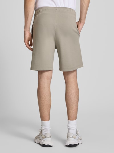 Męski model nosi Shorts mit Label-Stitching mit elastischem Bund von CHAMPION, bawełniany mix, krój regular fit, szerokość w rozmiarze M 37 cm, długość nogawki od kroku w rozmiarze M 42 cm, kolor jasnobeżowy, tekstura gładka, widok całej sylwetki z tyłu.