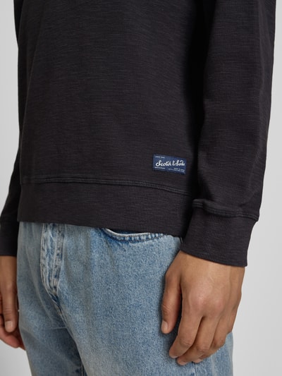 Männermodel trägt Regular Fit Sweatshirt mit Rundhalsausschnitt von Scotch & Soda, katoenmix, labeldetail, Nahaufnahme Oberkörper.