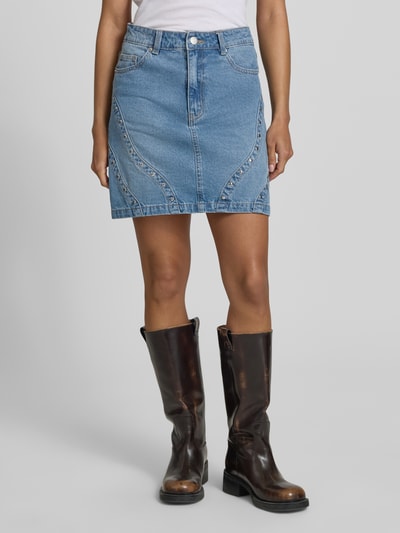 Frauenmodel trägt Jeansrock mit Nieten Modell 'CLIO' von YAS aus Reine Baumwolle, A-Linie, Minirock, Teilungsnähte, Ganzkörperansicht von vorne.