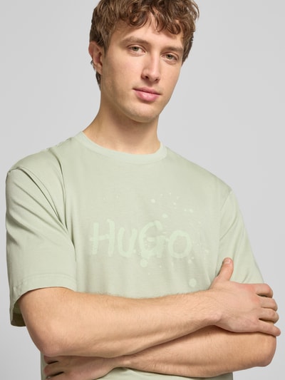 Męski model nosi Regular Fit T-Shirt aus reiner Baumwolle Modell 'NIEROFIX_U261' von HUGO, efekt: jednolity kolor, nadruk z motywem, wyhaftowane logo, okrągły dekolt, krótki rękaw, czysta bawełna, zbliżenie na górną część ciała.