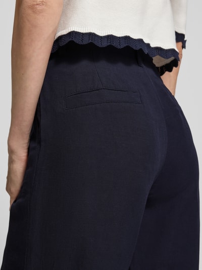 Frauenmodel trägt Wide Fit Stoffhose aus Viskose-Mix mit Leinen-Anteil von Marc Cain, dunkelblau mit Paspeltaschen, Detailaufnahme Rückansicht. Damen Stoffhose mit Logo-Detail, Eingrifftaschen, Bundweite bei Größe 36: 37 cm, Innenbeinlänge bei Größe 36: 82 cm.