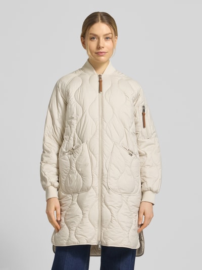 Frauenmodel trägt Steppmantel mit Ärmeltasche Modell 'AVON' von Beaumont Amsterdam in Beige, gerader Schnitt, Ganzkörperansicht von vorne.