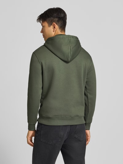 Männermodel trägt Regular Fit Hoodie aus Baumwoll-Mix mit Logo-Print von Alpha Industries, grün, glatte Textur, Ganzkörperansicht Rückansicht. Kontext: Herren Hoodie, Baumwoll-Mix, Regular Fit, Label am Saum, Kapuze mit Tunnelzug, langärmlig, elastische Abschlüsse, Rückenlänge 70 cm, Ärmellänge 64 cm.