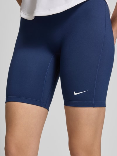 Frauenmodel trägt Radlerhose mit elastischem Bund und Logo von NIKE TRAINING, navyblau, körpernahe Passform, Nahaufnahme Oberkörper. Material-Mix mit Stretch-Anteil, Logo und elastischer Bund, Bundweite bei Größe S: 25 cm, Innenbeinlänge: 20 cm.