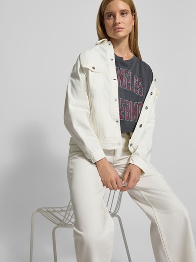 Vrouwenmodel draagt Cropped T-shirt met logo-print van Anine Bing, puur katoen, korte fit, logoprint, ronde hals, halflange mouwen, ruglengte maat S 47 cm, donkere kleuren met rode letters. Nahaufnahme Oberkörper.