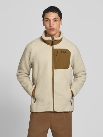 Männermodel trägt Fleecejacke mit Stehkragen von Helly Hansen in Beige mit braunen Details, lockere Passform, Ganzkörperansicht von vorne.