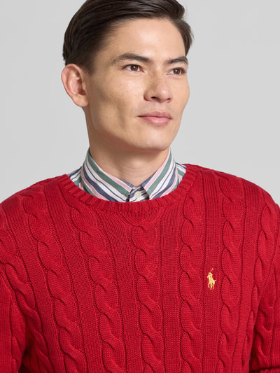 Männermodel draagt Strickpullover mit Label-Stitching van Polo Ralph Lauren in rood, ronde hals, regular fit, katoenen textuur. Nahaufnahme bovenlichaam.