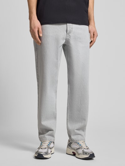 Männermodel trägt Loose Fit Jeans aus reiner Baumwolle Modell 'RUNNE' von Marc O'Polo Denim in heller Denim-Optik, 5-Pocket-Design, mit Nieten, Label-Patch, Knopf und verdecktem Reißverschluss, Ganzkörperansicht von vorne.